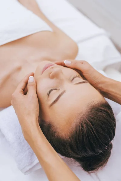 Mujer joven y relajada recibiendo masaje facial en el salón de spa - foto de stock