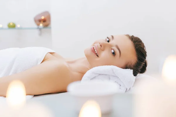 Happy young woman relaxing on massage table at spa — Stock Photo