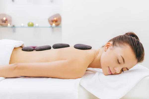 Hermosa joven que tiene terapia de piedra en el salón de spa — Stock Photo