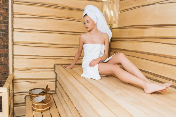 Beautiful young woman relaxing on bench at sauna — Stock Photo