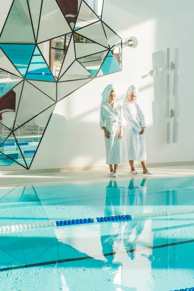 Attrayant jeunes femmes en peignoirs debout à côté de la piscine au centre de spa — Photo de stock