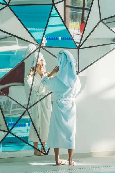 Jeune femme en peignoir et serviette regardant miroir dans le centre de spa — Photo de stock