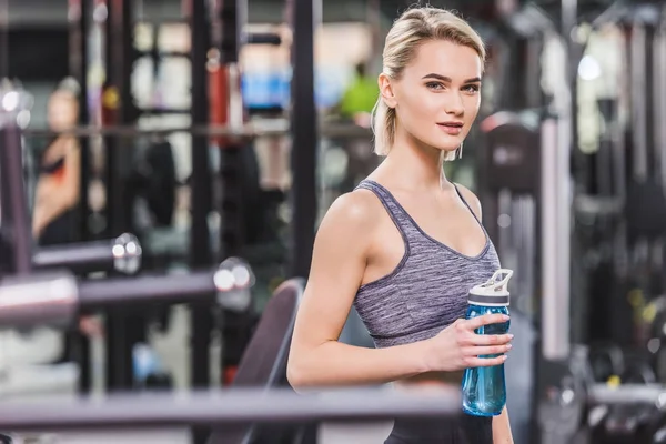 Hermosa joven con botella de agua en el gimnasio - foto de stock