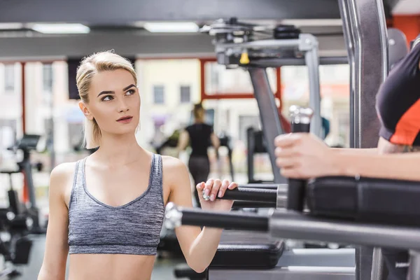 Junge Frau sieht andere Frau beim Training auf Fitnessgerät an — Stockfoto