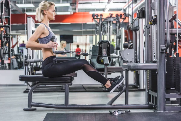 Side view of young woman working out with row machine at gym — Stock Photo