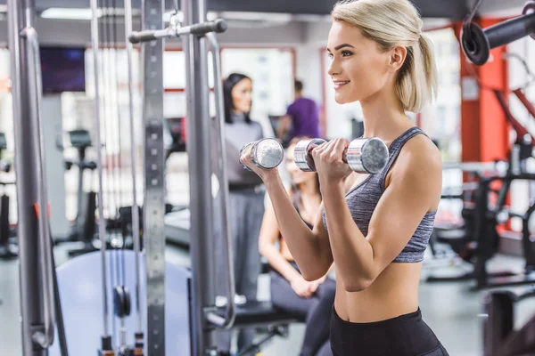 Attraktive junge Frau trainiert im Fitnessstudio mit Hanteln — Stockfoto