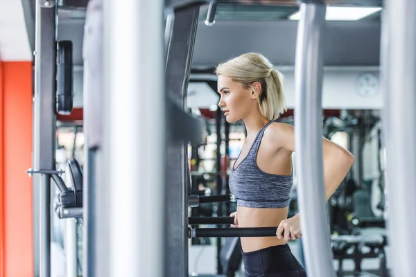 Attractive woman in modern sportswear doing exercise on push up bars at gym — Stock Photo