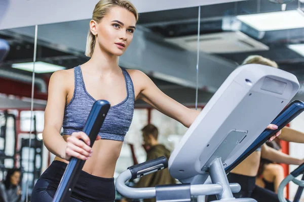 Beautiful sportive woman working out on elliptical machine at gym — Stock Photo
