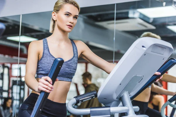 Schöne sportliche Frau, die im Fitnessstudio an einem Crossgerät trainiert — Stockfoto