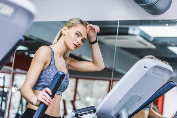 Mujer deportiva agotada haciendo ejercicio en la máquina elíptica en el gimnasio - foto de stock