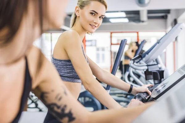 Primer plano de las mujeres deportivas que trabajan en máquinas elípticas en el gimnasio - foto de stock