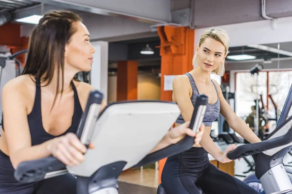 Beautiful sportive women working out on elliptical machines at gym — Stock Photo