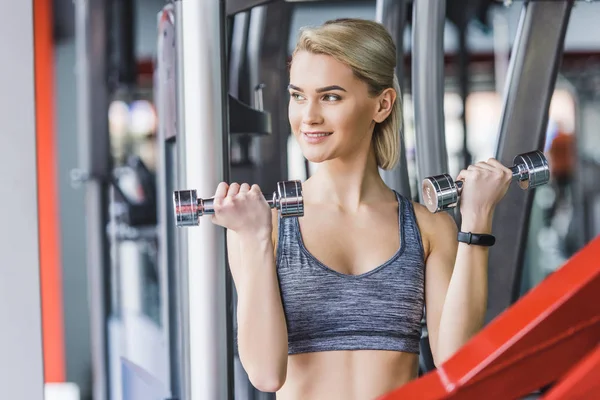 Smiling young woman working out with dumbbells at gym — Stock Photo