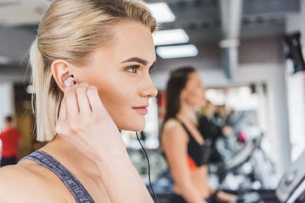 Retrato de cerca de una joven hermosa mujer escuchando música con auriculares en el gimnasio - foto de stock
