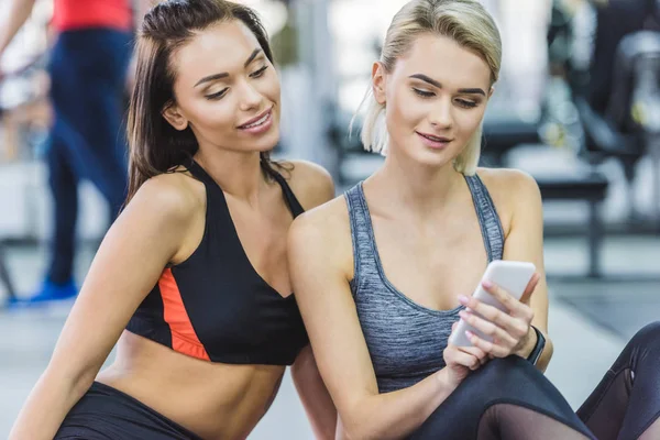 Junge sportliche Frauen nutzen Smartphone im Fitnessstudio — Stockfoto