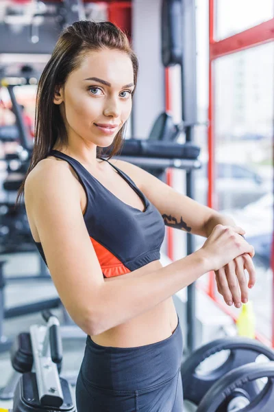 Junge sportliche Frau checkt Fitness-Tracker im Fitnessstudio und blickt in Kamera — Stockfoto