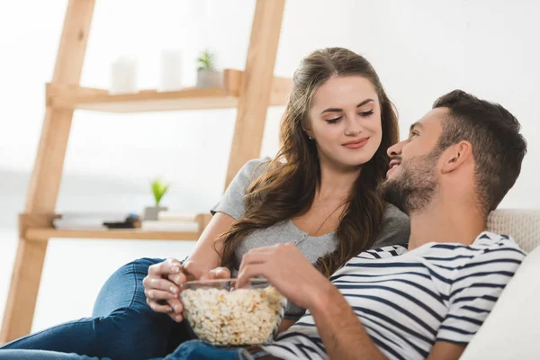 Jovem casal comer pipoca no sofá em casa — Fotografia de Stock