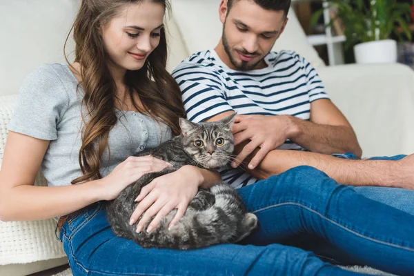 Hermosa joven pareja acariciando gato en casa mientras sentado en piso - foto de stock