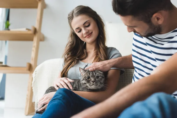 Glückliches junges Paar streichelt Katze zu Hause, während sie auf dem Boden sitzt — Stockfoto