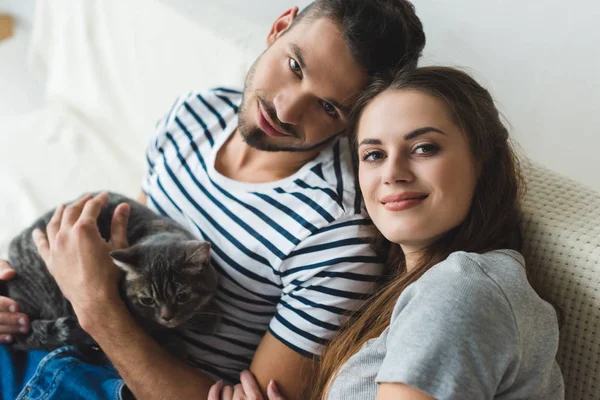 High angle view of beautiful young couple with adorable tabby cat sitting on couch — Stock Photo