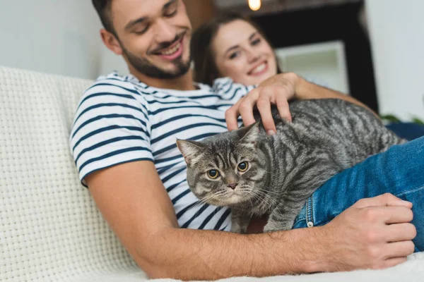 Happy young couple with adorable tabby cat sitting on couch — Stock Photo