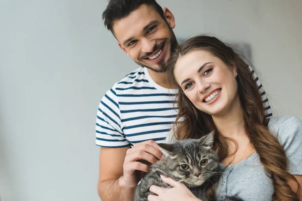Улыбающаяся молодая пара держит кота в руках и смотрит в камеру — стоковое фото