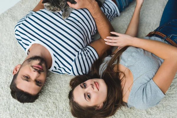 Vista superior do jovem casal deitado no chão com gato bonito tabby — Fotografia de Stock