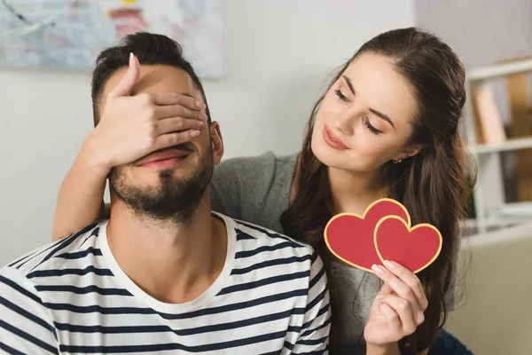 Jeune femme couvrant les yeux du petit ami avec la main et tenant la carte de voeux de la Saint Valentin — Photo de stock
