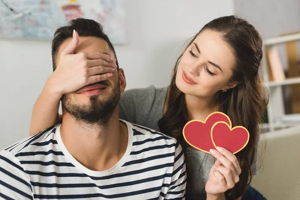 Mujer joven que cubre los ojos del novio con la mano y la celebración de la tarjeta de felicitación de San Valentín - foto de stock