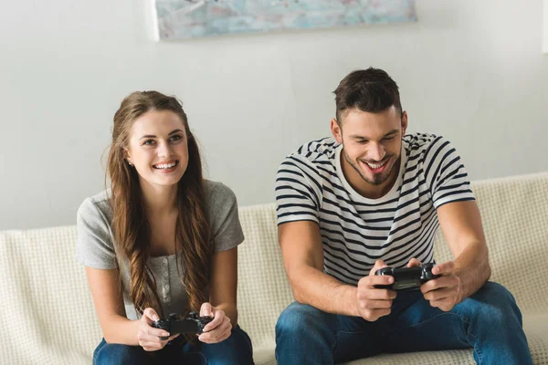 Smiling young couple playing games with gamepads at home — Stock Photo