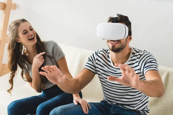 Ridendo giovane donna indicando il suo fidanzato utilizzando auricolare vr — Foto stock