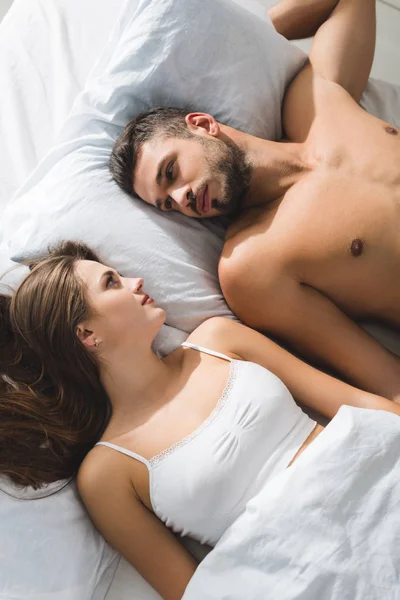 Вид сверху на молодую пару, лежащую в постели и смотрящую друг на друга утром — стоковое фото