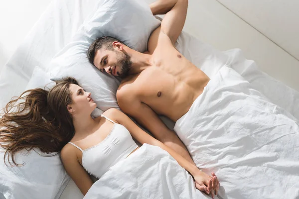 Вид сверху на молодую пару, держащуюся за руки в постели утром — стоковое фото