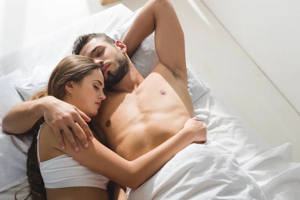 Vista superior de la joven pareja abrazándose en la cama por la mañana - foto de stock