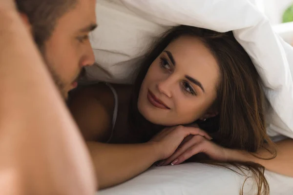 Junges Paar unter Decke schaut einander im Bett an — Stockfoto