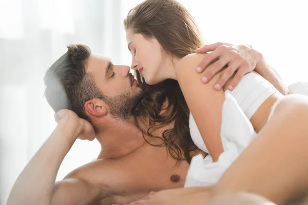 Hermosa pareja joven besándose en la cama en la mañana soleada - foto de stock