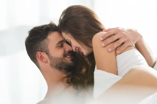 Joven pareja sonriendo y abrazándose en la cama por la mañana - foto de stock