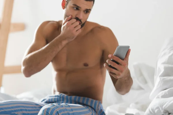 Потрясенный проспавший мужчина смотрит на смартфон в постели утром — стоковое фото