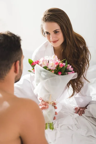 El hombre que presenta el ramo hermoso a la amiga en la mañana en la cama - foto de stock