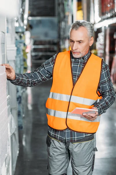 Travailleur âgé en gilet de sécurité en utilisant une tablette numérique dans l'entrepôt — Photo de stock