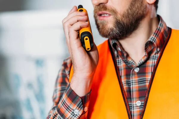 Vista ritagliata del lavoratore in giubbotto di sicurezza utilizzando walkie talkie — Foto stock