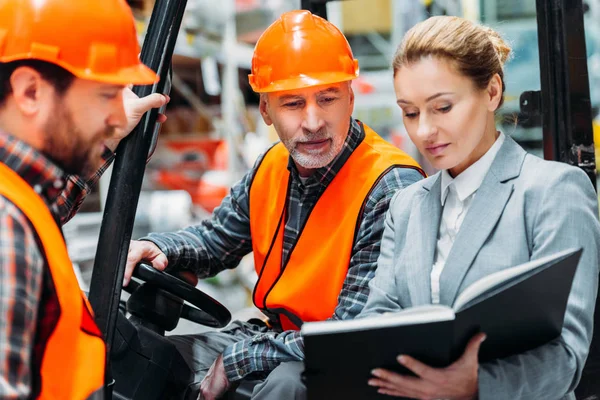 Dos trabajadores e inspector usando la máquina de la carretilla elevadora en almacén - foto de stock