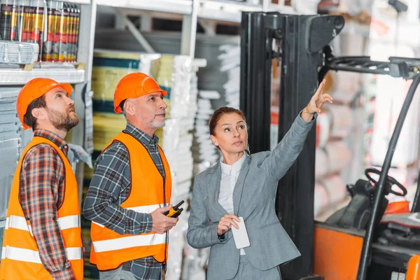 Inspector femenino mostrando algo a los trabajadores en el almacén - foto de stock
