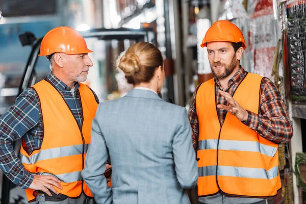 Male workers in safety vests and helmets talking with inspector in storehouse — Stock Photo