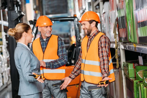 Male workers in safety vests and helmets talking with inspector in storehouse — Stock Photo