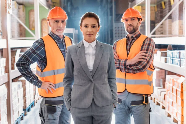 Trabajadores en cascos e inspector en traje posando en almacén - foto de stock