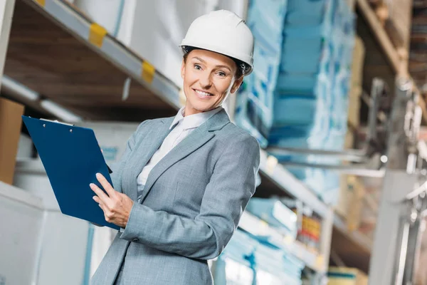 Kommissarin im Helm schreibt Notizen auf Klemmbrett im Lager — Stockfoto