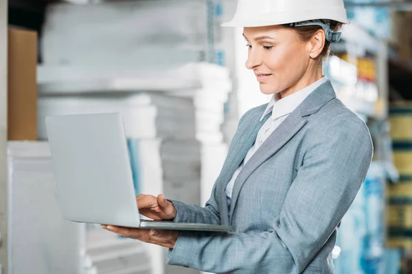 Female inspector in helmet with laptop in warehouse — Stock Photo