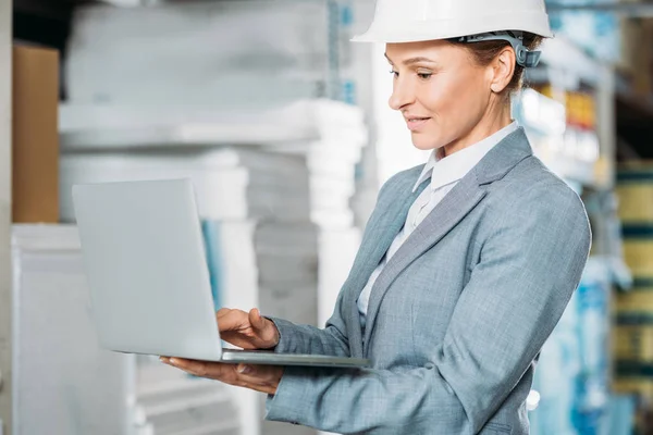 Kommissarin mit Helm und Laptop in Lagerhalle — Stockfoto