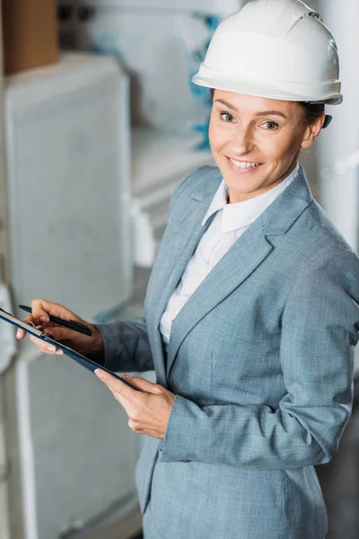 Kommissarin im Helm schreibt Notizen auf Klemmbrett im Lager — Stockfoto